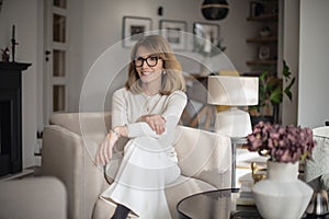 An attractive mid aged woman sitting in her modern home and relaxing in an armchair