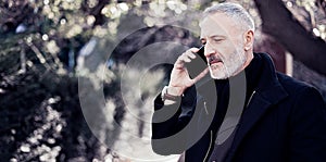 Attractive middle age businessman calling smartphone while spending time in a urban park.Horizontal wide,blurred