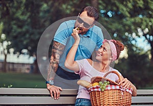 Attractive middle age couple during dating, enjoying a picnic on a bench in the city park.