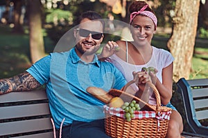 Attractive middle age couple during dating, enjoying a picnic on a bench in the city park.