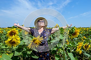 Attractive middle age woman in straw hat with arms outstretched in sunflower field, celebrating freedom. Positive emotions feeling