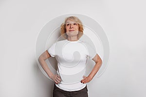 Attractive middle age woman wearing casual t-shirt looking up and standing against white studio wall background