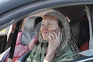 An attractive middle aged Asian smiling woman sitting in a car talking on the phone
