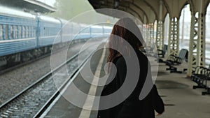 Attractive middle-aged brunette woman in a black coat at the railway station. It`s raining. Close-up of walking legs in