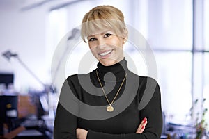 Attractive middle aged businesswoman looking at camera and smiling while standing at the office