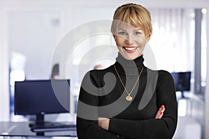 Attractive middle aged businesswoman looking at camera and smiling while standing at the office