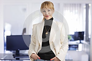 Attractive middle aged businesswoman looking at camera and smiling while standing at the office