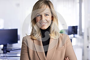 Attractive middle aged businesswoman looking at camera and smiling while standing at the office