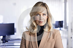 Attractive middle aged businesswoman looking at camera and smiling while standing at the office