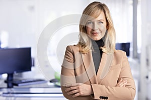 Attractive middle aged businesswoman looking at camera and smiling while standing at the office