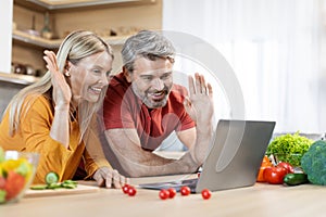 Attractive middle aged couple cooking and using laptop at kitchen