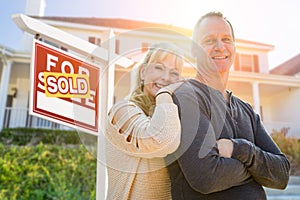 Attractive Middle-aged Couple In Front House and Sold Real Estate Sign