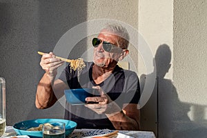 attractive middle-aged man have fun while eating sitting at a table laid Chinese take away food