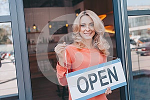 attractive middle aged small business owner holding sign open and smiling