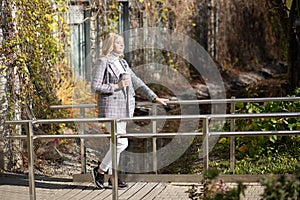 Attractive middle-aged woman in checkered jacket and grey roll-neck sweater stand luxuriating in warm autumn sunshine.