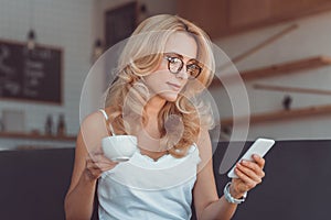attractive middle aged woman drinking coffee and using smartphone