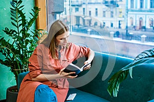 Attractive middle aged woman enjoying reading book, sitting on sofa in her