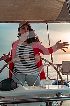 Attractive middle-aged woman at the helm of a yacht on a summer day. Luxury summer adventure, outdoor activities.