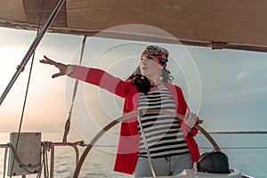 Attractive middle-aged woman at the helm of a yacht on a summer day. Luxury summer adventure, outdoor activities.