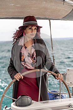 Attractive middle-aged woman at the helm of a yacht on a summer day. Luxury summer adventure, outdoor activities.