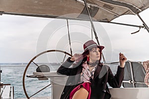 Attractive middle-aged woman at the helm of a yacht on a summer day. Luxury summer adventure, outdoor activities.