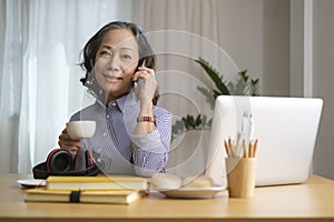 Attractive middle aged woman holding coffee drinking coffee and talking on a cell phone, having pleasant conversation