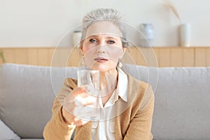 Attractive middle aged woman holding glass of water and looking at camera. Healthy lifestyle
