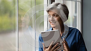 Attractive middle-aged woman holding tablet looking out the window