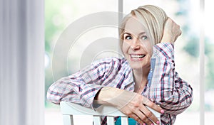 Attractive middle-aged woman looking relaxed at the camera, sitting near the window. The beautiful face close up