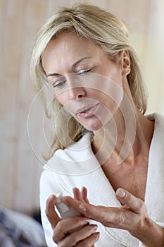 Attractive middle-aged woman putting cream on her face