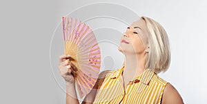 Attractive middle aged woman relaxing with fan. Mature woman experiencing hot flush from menopause isolated