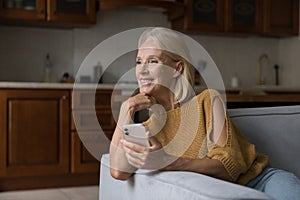 Attractive middle-aged woman resting on sofa at home with smartphone