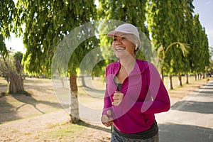 Attractive middle aged woman running happy at city park . beautiful and sporty lady on her 40s exercising doing jogging workout on