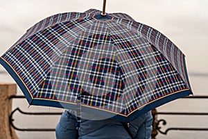 Attractive middle-aged woman sitting from behind in the rain with an umbrella in front of Lake Maggiore