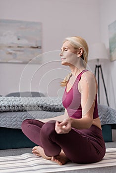 attractive middle aged woman sitting in lotus position on yoga mat