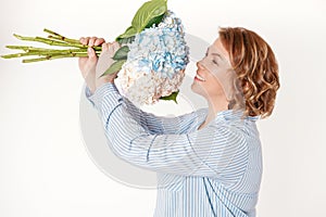 Attractive middle-aged woman smiling and holding bouquet of hydrangea flowers. Concept holiday