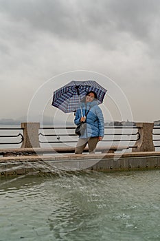 Attractive middle-aged woman standing in the rain in front of a fountain on the lakeside promenade