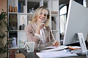 Attractive middle aged woman working at office, using contemporary desktop computer.