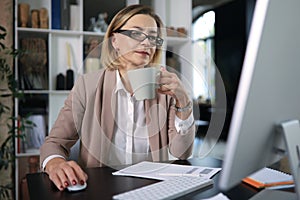 Attractive middle aged woman working at office, using contemporary desktop computer.