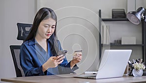 Attractive millennia Asian female holding her smartphone and credit card, using mobile banking app or online shopping photo