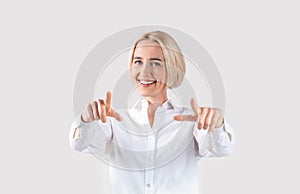 Attractive millennial businesswoman pointing at camera on light grey studio background