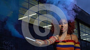 Attractive mixed-race girl clubbing in cloud of blue smoke, self-expression