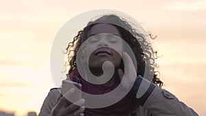 Attractive mixed race woman listening to music, dancing in trance at sunset