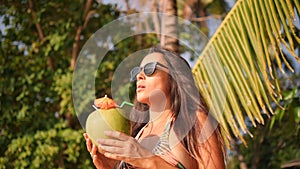 Attractive Mixed Race Young Tourist Woman Drinking Fresh Thai Coconut Water Cocktail at Tropical Beach. 4K, Slowmotion