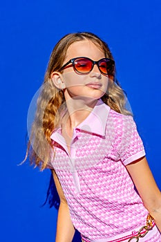 Attractive model Barbie style girl wearing sunglasses, pink tee-shirt and shorts with long hair on blue backdrop