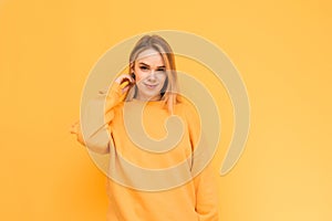 Attractive model in an orange sweater poses on, smiles and looks into the camera, isolated on a yellow background. Positive lady