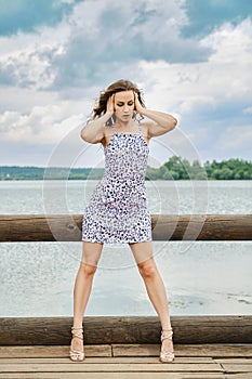 Attractive model in patterned sundress posing on wooden pier