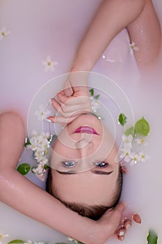 An attractive model takes a bath with milk and apple petals.