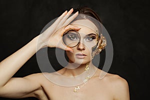 Attractive model woman with fashionable makeup holding gold bracelet on black background