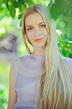 Attractive modest young girl with blond dren hair and natural make-up in purple dress outdoors, tenderness and softness on nature